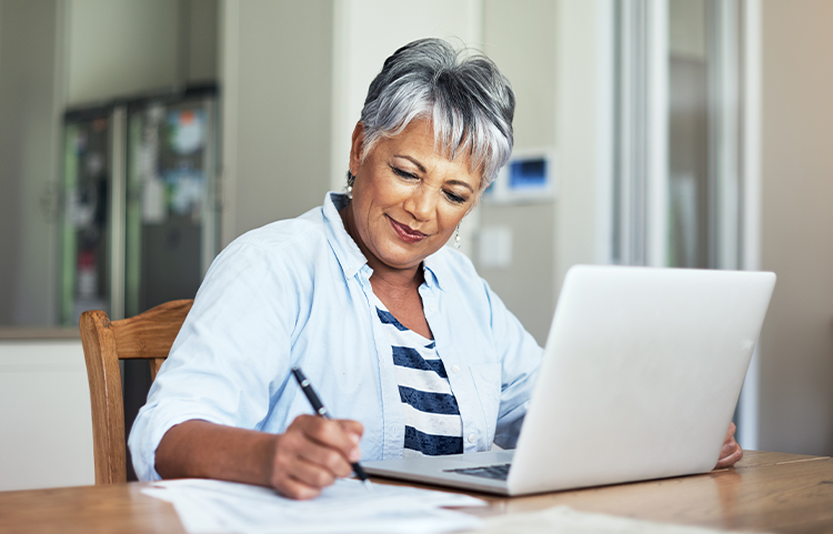 Woman looks at her computer while writing down something on a piece of paper